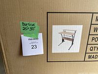 Photo of sealed cardboard box containing the computer desk, showing label with image and approximate box size 25" x 30".