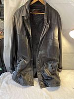 Front view of black Daniel leather coat on hanger, showing collar, buttons, side pockets, and quilted lining inside.