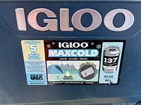 Close-up of the front label of the cooler showing brand Igloo, MaxCold model, 85L capacity, 137 can capacity, and features.