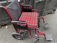 Side view of the folding wheelchair showing the red tartan padded seat, armrests, footrests and wheels.