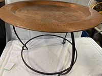 Full view of round hammered copper top side table with visible black cast iron base.