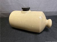 Beige glazed ceramic water bottle or bed warmer, horizontal position showing body and spout with knob end, Bakelite stopper on top.