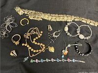 Overview photo of assorted jewelry pieces including bracelets, rings, necklaces, and brooches laid on black cloth