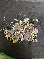 Bag of assorted costume jewelry pins, earrings, brooches and other small pieces spread out on dark surface.