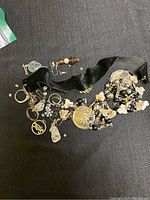 Assorted costume jewelry spread out on black surface showing detailed views of earrings, a black velvet choker necklace with attached decorations, and other pieces with beads and floral charms.