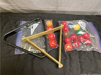 Photo of two sets of assorted pool balls partially inside two plastic bags with one black plastic triangle rack and one wooden triangle rack beside them on a dark surface.