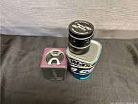 Three Bluetooth speakers placed on a black cloth. Varied shapes and colors, some with logos visible.