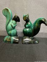 Front view of both squirrel bookends side by side showing glossy green and brown ceramic finish and curved bushy tails.