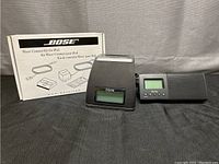 Photo showing the Bose Wave Connect Kit for iPod box, the black adapter piece, and two iHome clock radios on a black fabric surface.