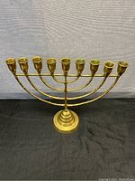 Front view of solid brass menorah showing all 9 candle holders, stepped base, and overall structure.