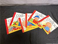 Photo showing four Caillou book covers with red spines and colorful illustrations including the character Caillou engaged in various activities.