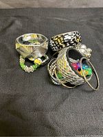 Photo showing assorted costume bracelets including silver-tone bangles, a black and silver patterned bangle, multi-colored beaded bracelets, and chain-link designs.