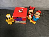 Three vinyl figurines (Mickey, Minnie, Pluto) arranged with the red Movie Motion Zoetrope box on black surface.