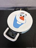 Closed Olaf waffle maker showing the white lid with Olaf's smiling face printed in color.