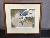 Framed artwork showing two Blue Jays in a winter setting, snow-covered branches, wooden frame, matted.