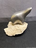 Side view of the smooth pewter polar bear sculpture mounted on a rough limestone base, showing profile with head raised.