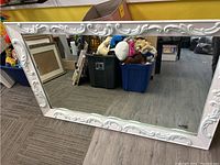 Full view of large rectangular mirror with white ornate heavy frame showing floral and scroll raised decorations along edges.