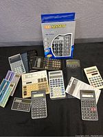 Overview of all 13 calculators of various brands and styles laid out on a black cloth with original Xinnuo box in background.