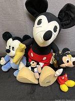 Four Mickey Mouse plush toys arranged on a black surface showing different sizes and styles