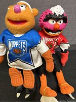 Frontal view showing Animal in red hockey jersey and Fozzie Bear in blue hockey jersey, both wearing white helmets.