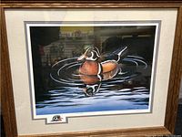 Framed lithograph showing a colorful duck on water with ripples, in a wooden frame with light mat.