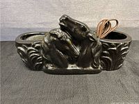 Front view of black ceramic lamp showing detailed horse heads and two candle holder slots.