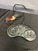 Photo of vintage black Maxx 6 in 1 Casino Game controller with directional pad, buttons A, B, arrow buttons, start, select, reset buttons, and AV cable with red and yellow connectors coiled beside it.