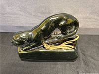 Side view of black ceramic panther desk lamp showing sleek crouching panther figure on rectangular base with attached electrical cord.