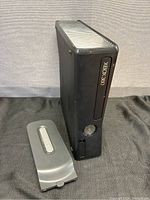 Front right angled view of black Xbox 360 console standing vertically with detachable 120 GB hard drive next to it on black surface.