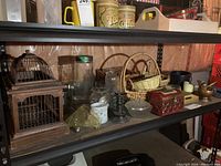 Photo of shelving unit holding bird cage, wicker baskets, glass vases, candle holders, decorative boxes and containers.