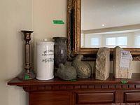Full view of all six items on mantle showing candlestick, ceramic jar, stone vase, two stone bird figurines, and two stone bookends.