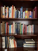 Bookshelf with three shelves containing a variety of hardcover and paperback books including art and dictionary titles.