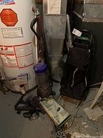 Dyson DC66 vacuum with attachments and black shopper buggy, placed near a water heater in a basement.