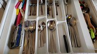 Drawer with organized stainless steel flatware, including forks, spoons, and knives, alongside some kitchen utensils