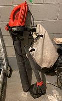 Full view of Black and Decker Vortex BV2500 yard vacuum with fabric debris bag and two nozzle attachments displayed in a garage setting.