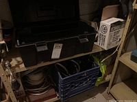 Black plastic toolbox on shelf with labeled sticker, ROMEX wire box on the right, and blue milk crate below containing cables and wires