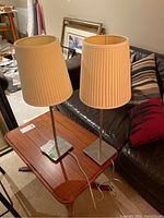 Two matching metal base table lamps with cream pleated fabric shades standing on a wooden table in a basement.