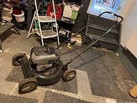 Side and partial top view of the black Murray gas lawn mower on interlocking foam mats showing overall condition and structure.