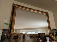 Front view of large rectangular beveled edge mirror in ornate gold and black painted wooden frame placed above a shelf with decorative items.