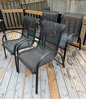 Four black outdoor armchairs on wooden deck, showing metal frames and mesh seats and backs