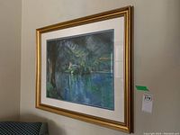 Full view of the framed print hung on a wall, showing the gold painted wooden frame and part of the dark-toned print inside.