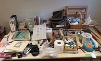 Photo showing a variety of quilting supplies including books, threads, tools, rulers, baskets, and fabrics packed together on a table.