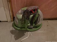 Green Bissell Little Green spot steam cleaner with clear tanks and coiled hose visible from the front angle