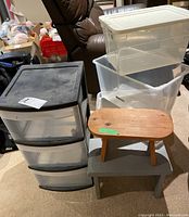 Full view of four-drawer plastic storage bin, three additional plastic storage bins with one lid, and two wooden step stools stacked together.