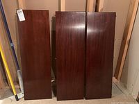 Three wooden table leaves standing vertically showing smooth dark brown finish and size