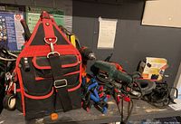 Multiple power tools and hand tools displayed on a shelf next to a black and red Husky tool bag with pockets and shoulder strap.