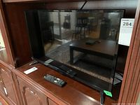 Front view of the Insignia 31-inch LED TV sitting on a wooden cabinet with two remote controls placed in front of it.