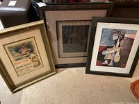 Three framed artworks side by side on floor including a large framed sculptural art piece, Moulin Rouge poster reproduction, and a cubist art reproduction.