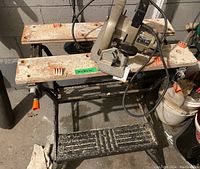 View of Black and Decker Workmate 300 collapsible work bench with circular saw mounted or placed on top. Shows rust, wear, black plastic platform at foot level.