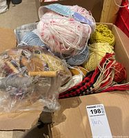 Box containing multiple skeins of yarn in various colors and a bag of wooden knitting tools.